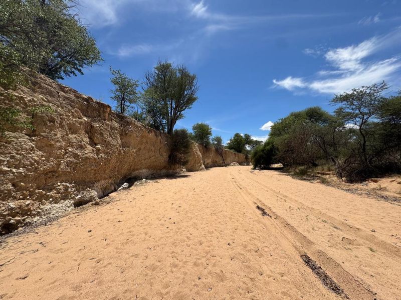 A scenic view of a dry riverbed landscape featuring natural sandy terrain and rocky embankments on a farm property.