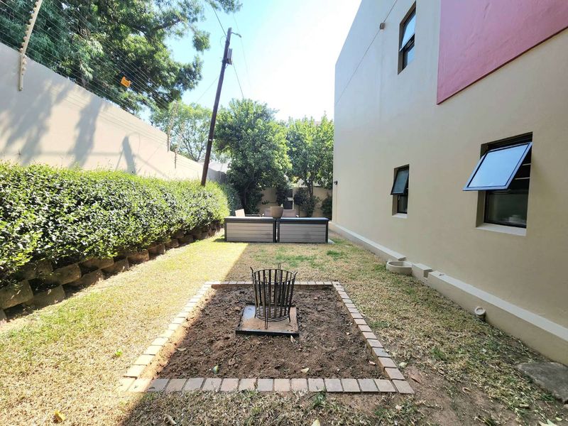 A rear garden area featuring a brick-edged fire pit, manicured hedge, and secure boundary wall with electric fencing.