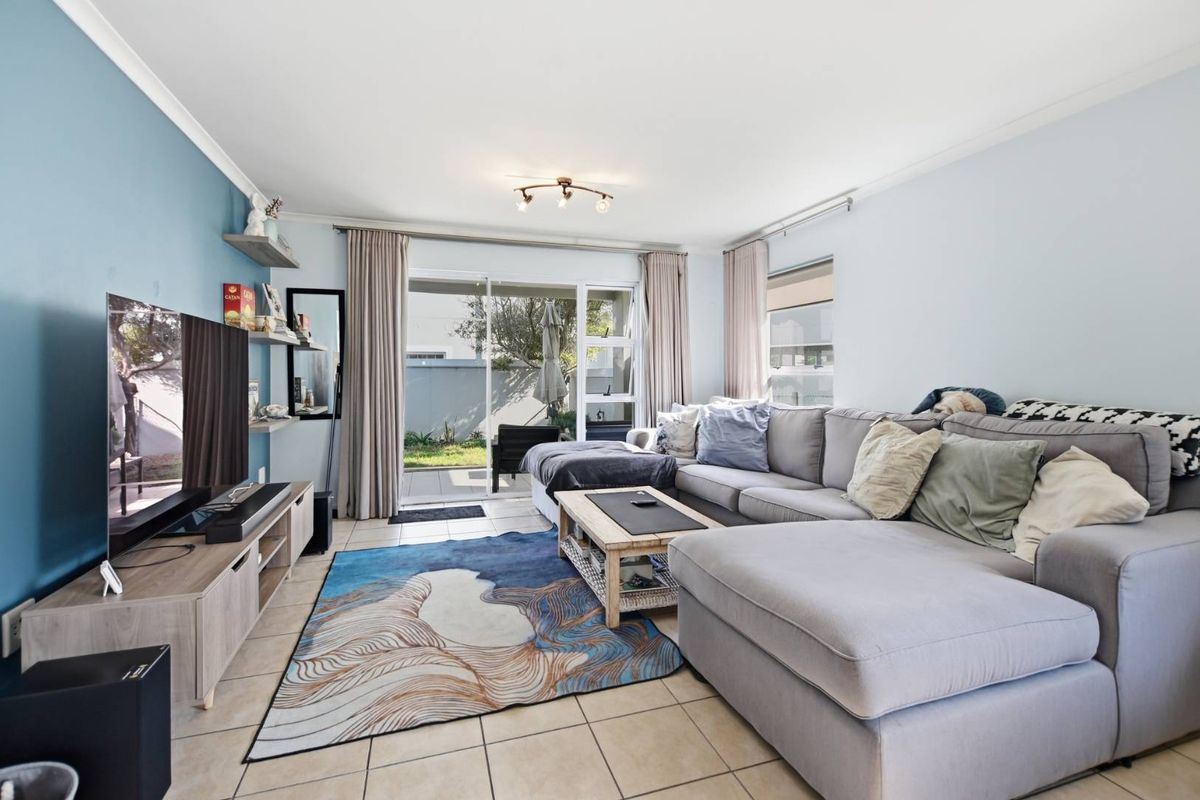 A bright and comfortable living room featuring tiled flooring, a feature wall, and large sliding glass doors providing access to the outdoor patio area.