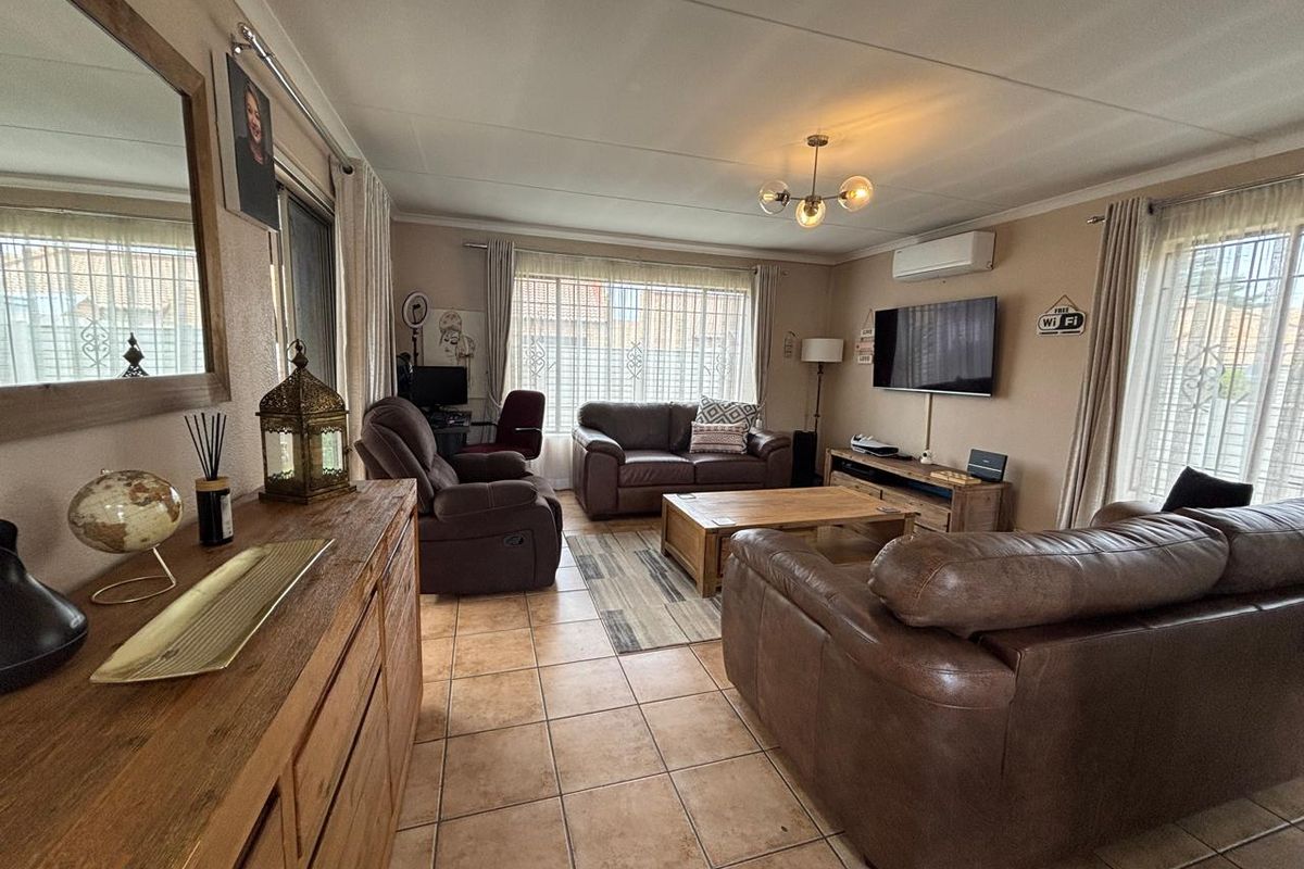 A spacious living room featuring tiled flooring, large windows with security bars, and a wall-mounted air conditioning unit.