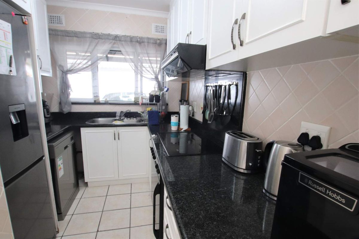 A functional galley-style kitchen featuring white cabinetry, dark granite countertops, a built-in hob, extractor fan, and stainless steel sink.