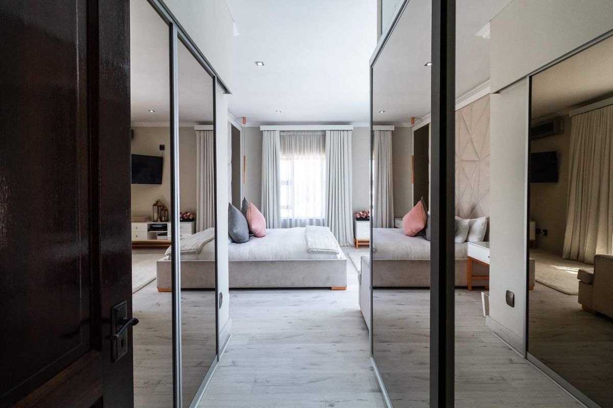 Spacious bedroom featuring light laminate flooring, recessed downlighting, and extensive mirrored built-in wardrobes, creating a bright and modern atmosphere.