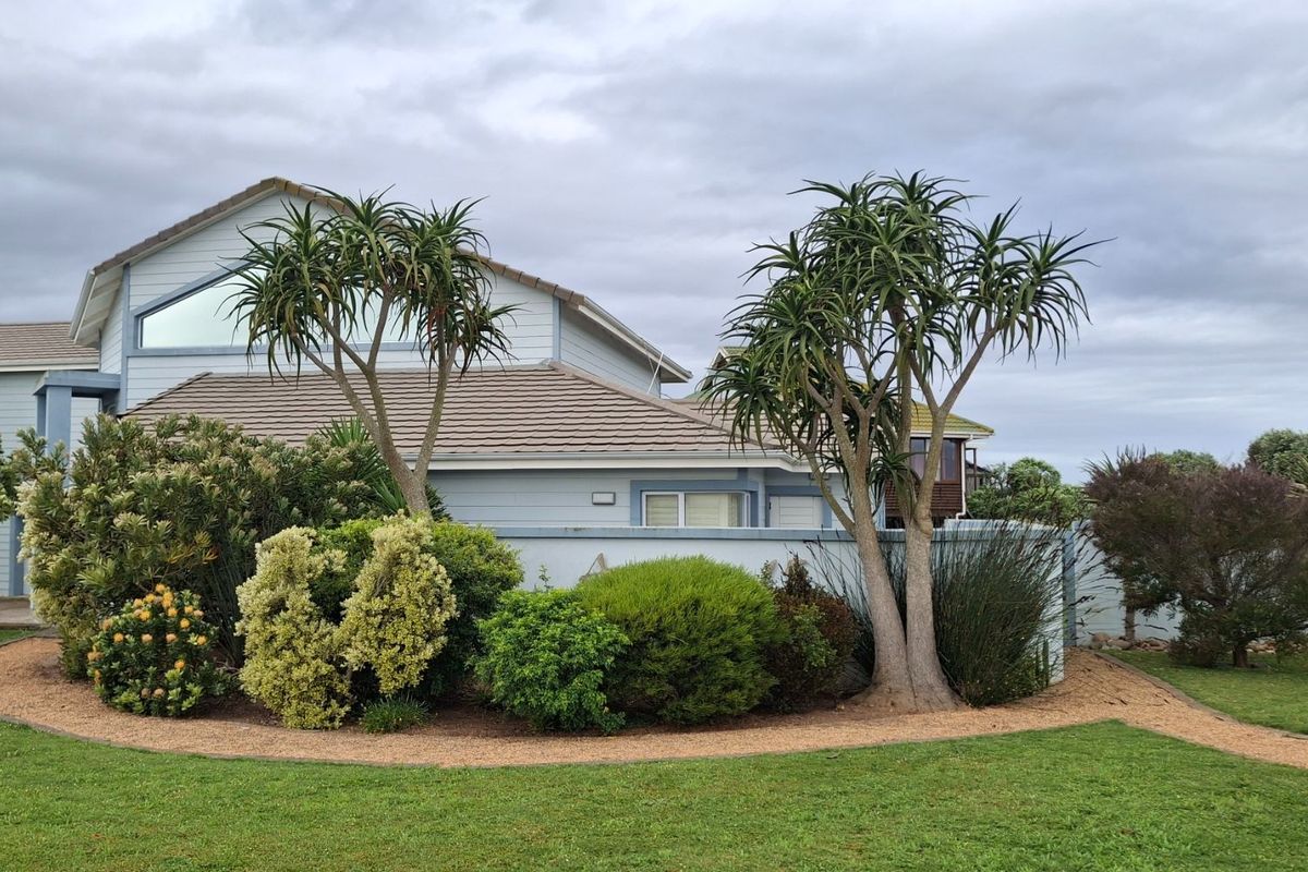 A well-maintained rear exterior view of the house featuring weatherboard cladding, a tiled roof, and established garden landscaping.