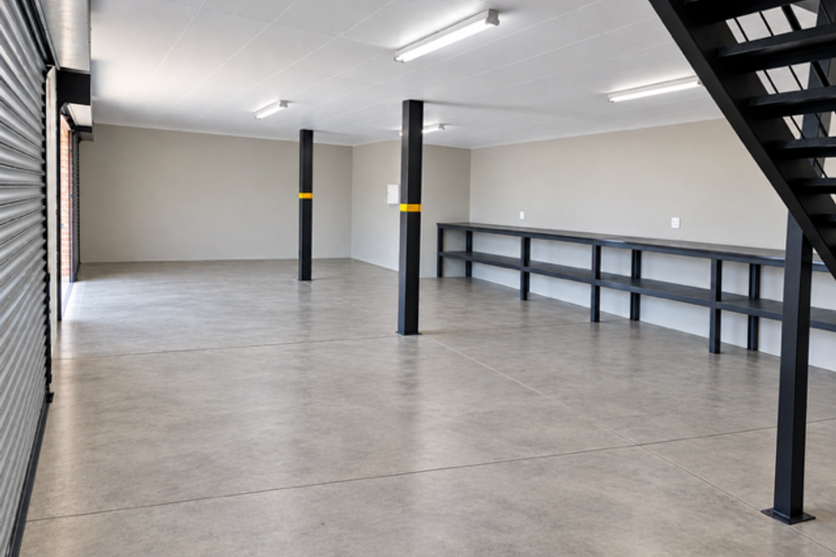 Spacious industrial garage featuring polished concrete floors, built-in steel shelving, a modern staircase, and high-clearance roller shutter access.
