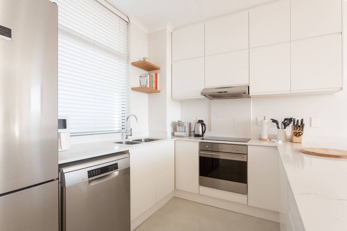 Modern kitchen featuring white cabinetry, stone countertops, integrated stainless steel oven, hob, extractor fan, and double sink with venetian blinds.