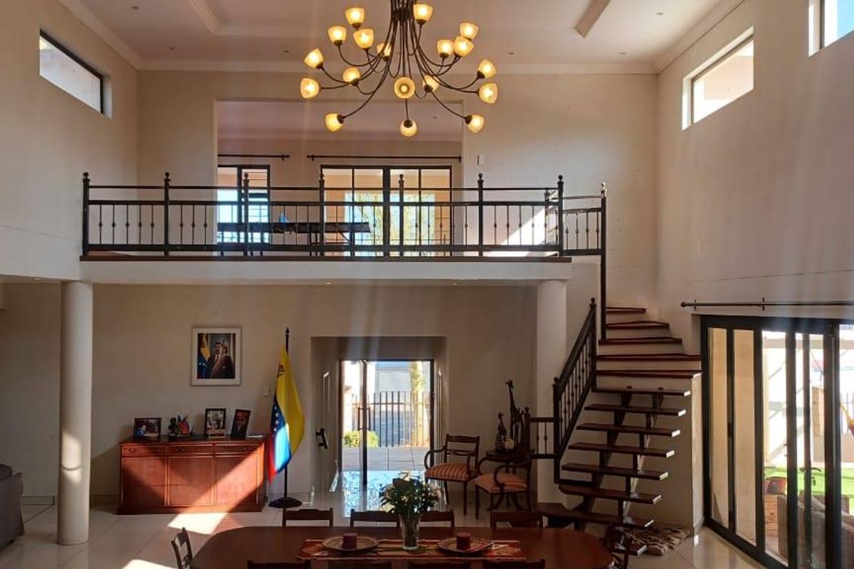 Spacious double-volume living area featuring a mezzanine level, wrought iron staircase, large sliding glass doors, and elegant recessed lighting.