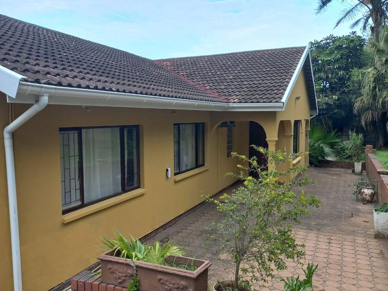 A rear view of the house featuring a paved patio area, brick retaining wall, and concrete tiled roof with an integrated gutter system.