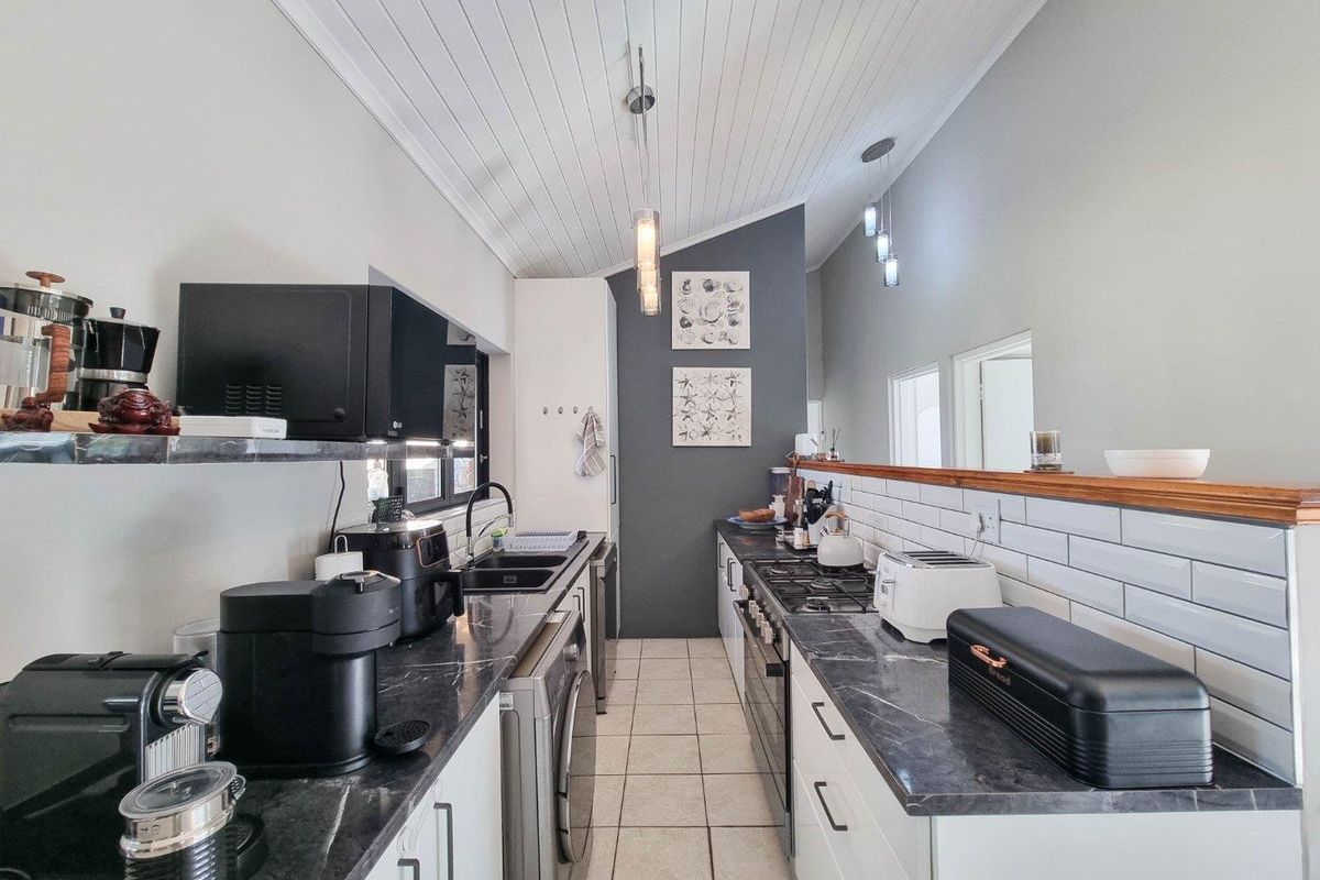 Modern galley-style kitchen featuring dark stone countertops, white cabinetry, subway tile backsplash, gas hob, and vaulted tongue-and-groove ceiling.