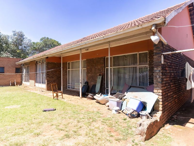 Rear view of a brick house featuring a covered patio area, large windows, and a spacious backyard.