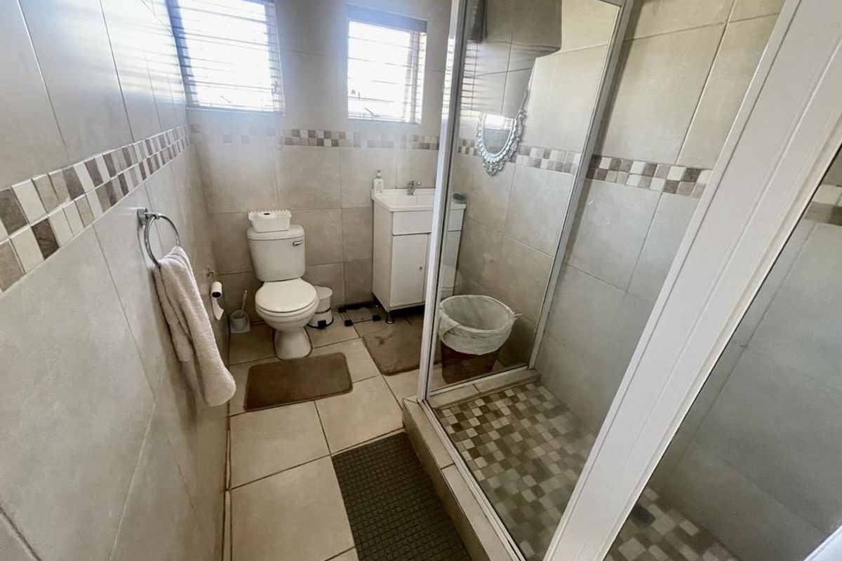A functional bathroom featuring a glass-enclosed shower, a pedestal vanity, and neutral wall and floor tiling.