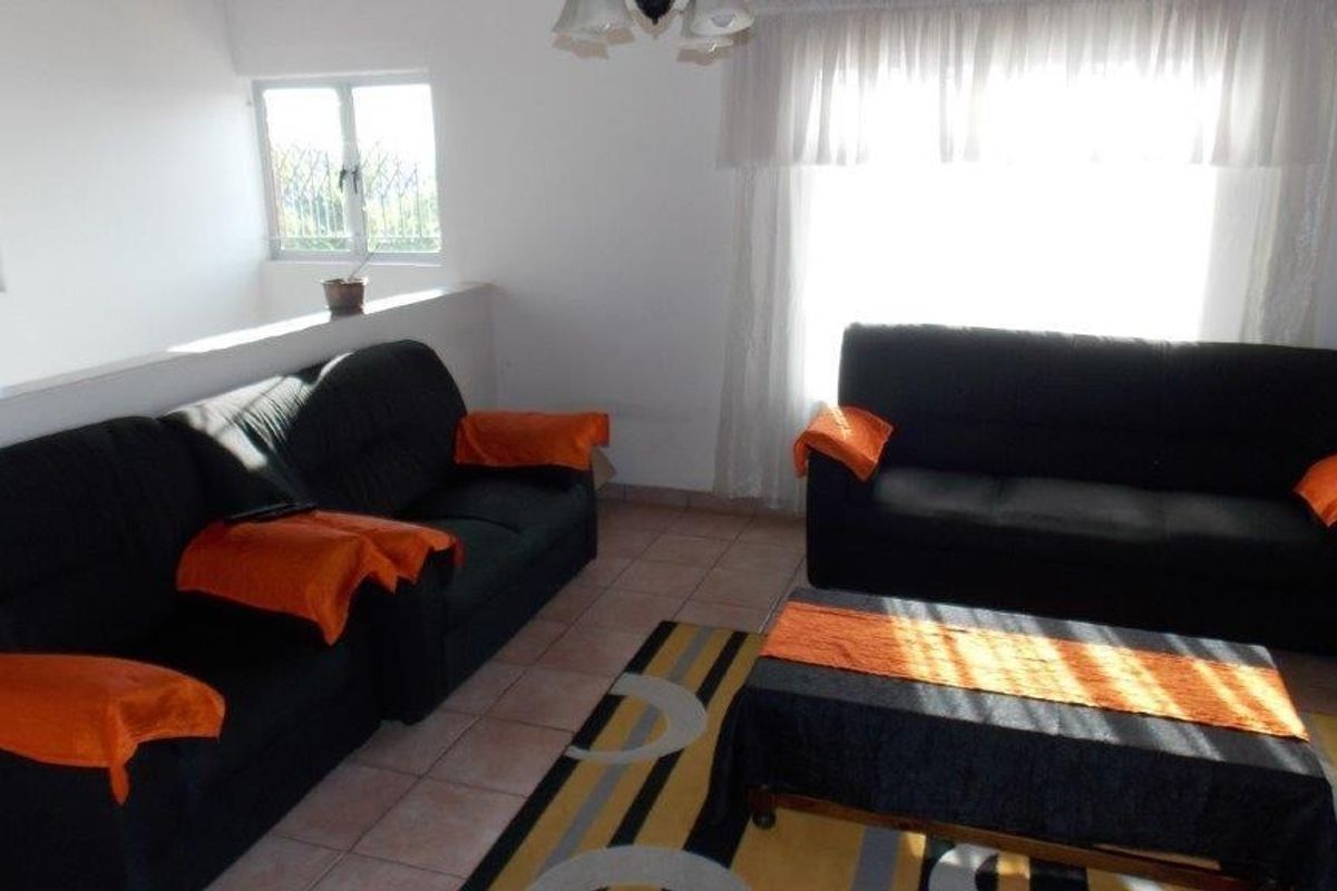 A living room area featuring tiled flooring and windows fitted with security bars, offering a functional space with natural light.