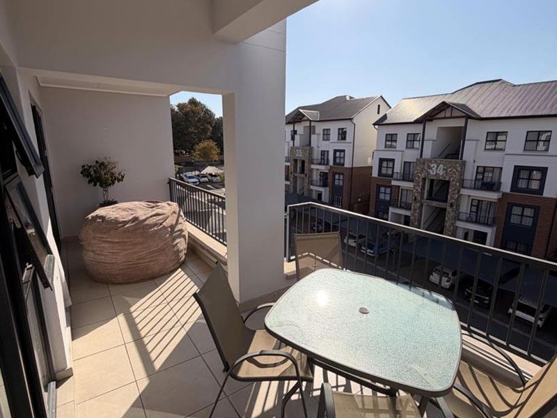A covered balcony featuring tiled flooring and a metal balustrade, offering an outdoor space with views of the surrounding apartment complex.