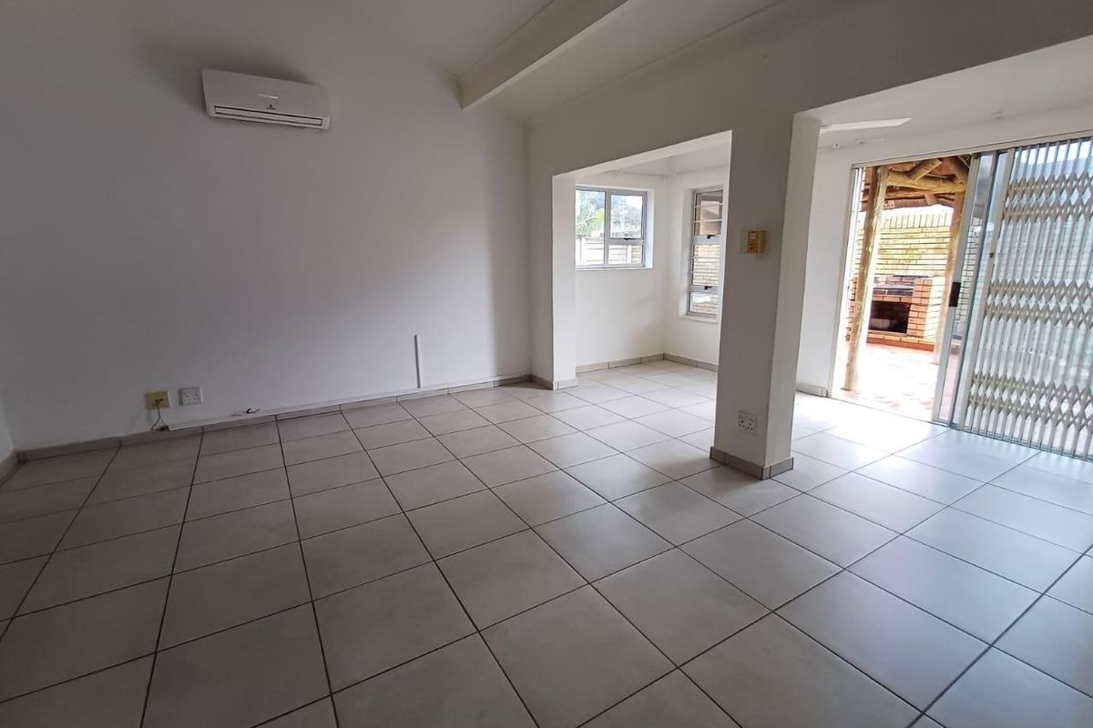 Spacious, open-plan living area featuring neutral tiled flooring, a wall-mounted air conditioning unit, and direct access to an outdoor patio area.