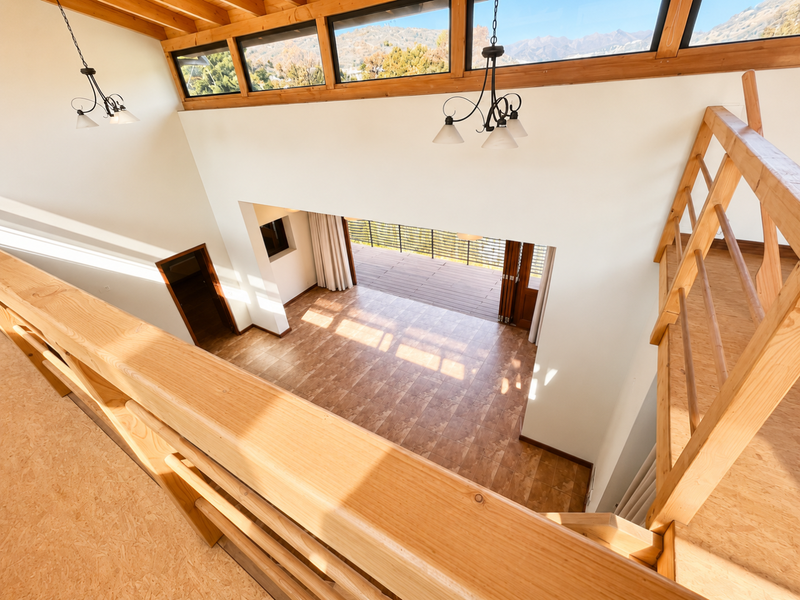 Spacious double-height living area featuring timber mezzanine railing, exposed ceiling beams, clerestory windows, and seamless access to an outdoor deck through bi-fold doors.