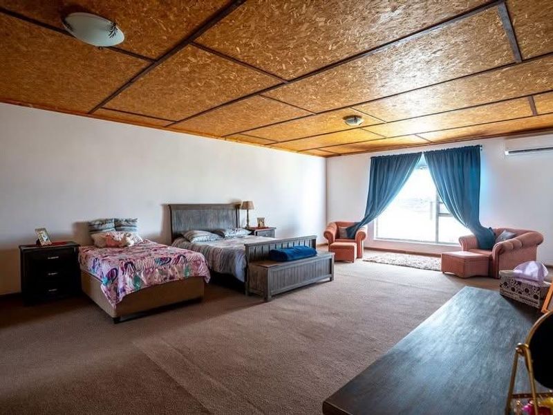 Spacious bedroom featuring carpeted flooring, a split-system air conditioner, and a distinctive OSB panel ceiling.