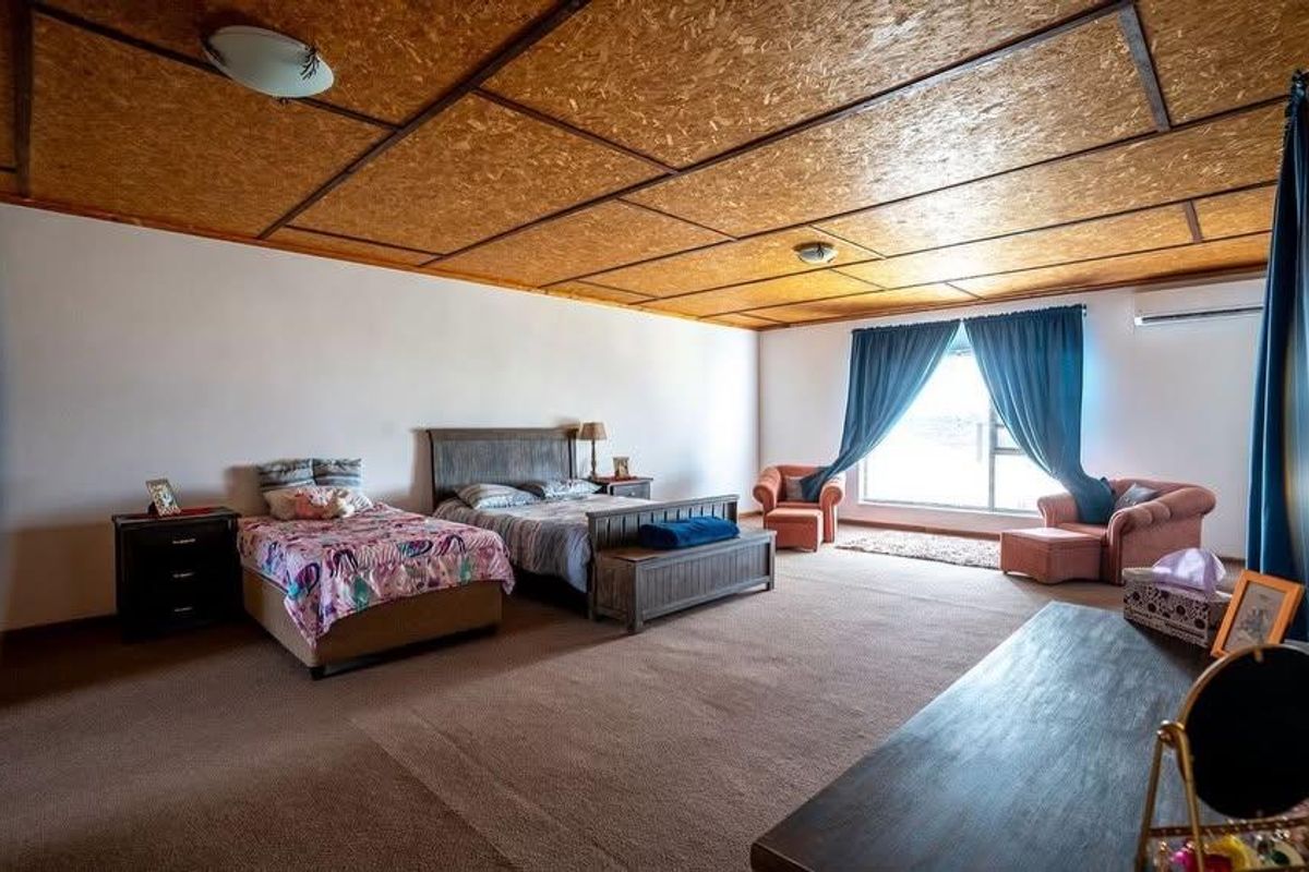 Spacious bedroom featuring carpeted flooring, a split-system air conditioner, and a distinctive OSB panel ceiling.