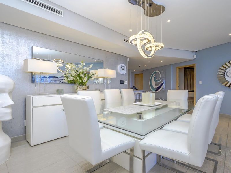 A modern, well-maintained dining room featuring tiled flooring, recessed ceiling lighting, ducted air conditioning, and a stylish feature wall.