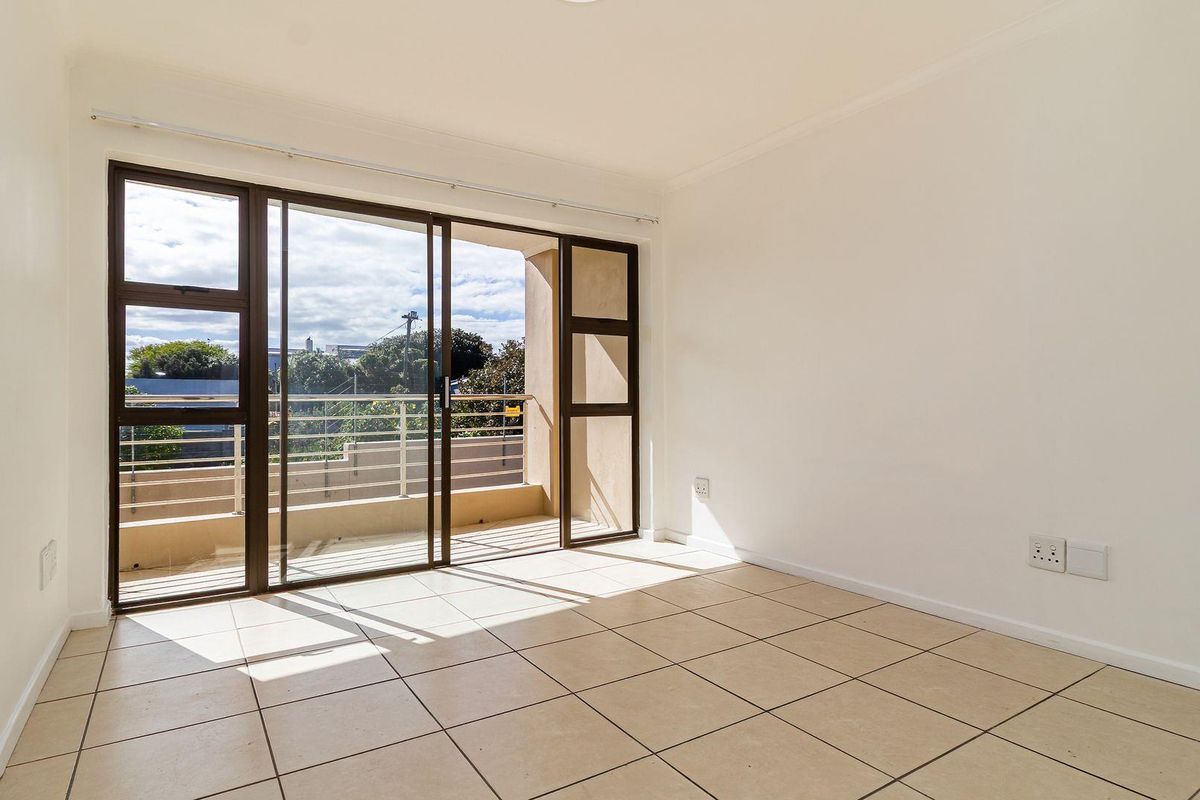 A bright, empty bedroom featuring neutral tiled flooring and large sliding glass doors that provide direct access to a private balcony.