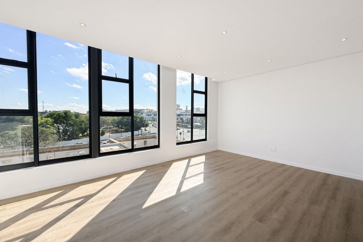 A bright, modern, and empty living area featuring large black-framed windows, recessed downlights, and high-quality laminate wood flooring with an urban view.
