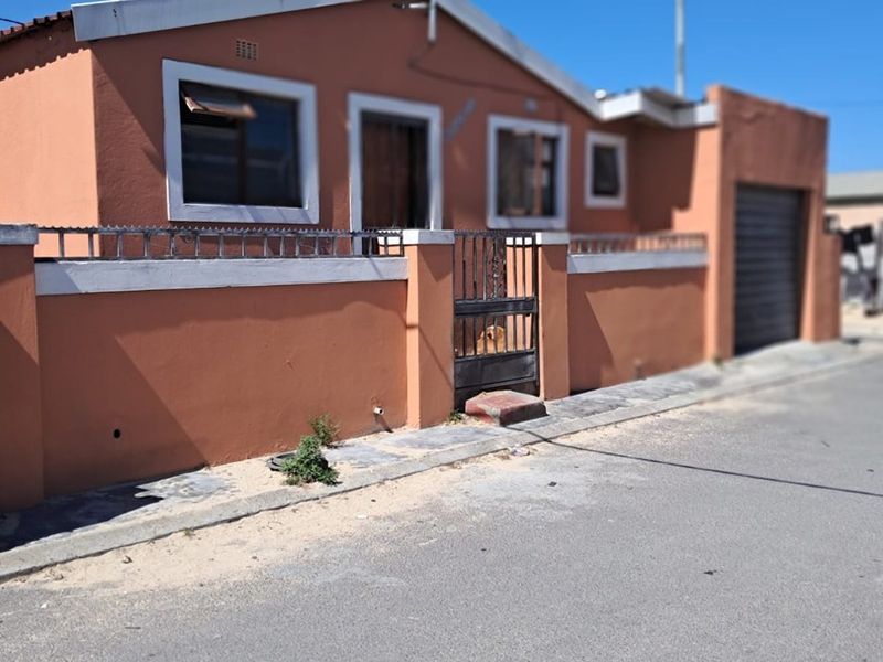 Front exterior view of a single-story house featuring a perimeter wall, metal security gate, and attached garage.