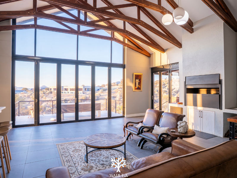 Spacious living room featuring a vaulted ceiling with exposed timber trusses, large glass folding doors, and a built-in fireplace with scenic views.