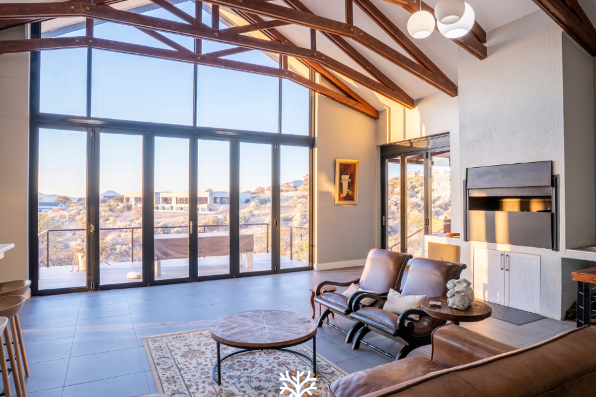 Spacious living room featuring a vaulted ceiling with exposed timber trusses, large glass folding doors, and a built-in fireplace with scenic views.
