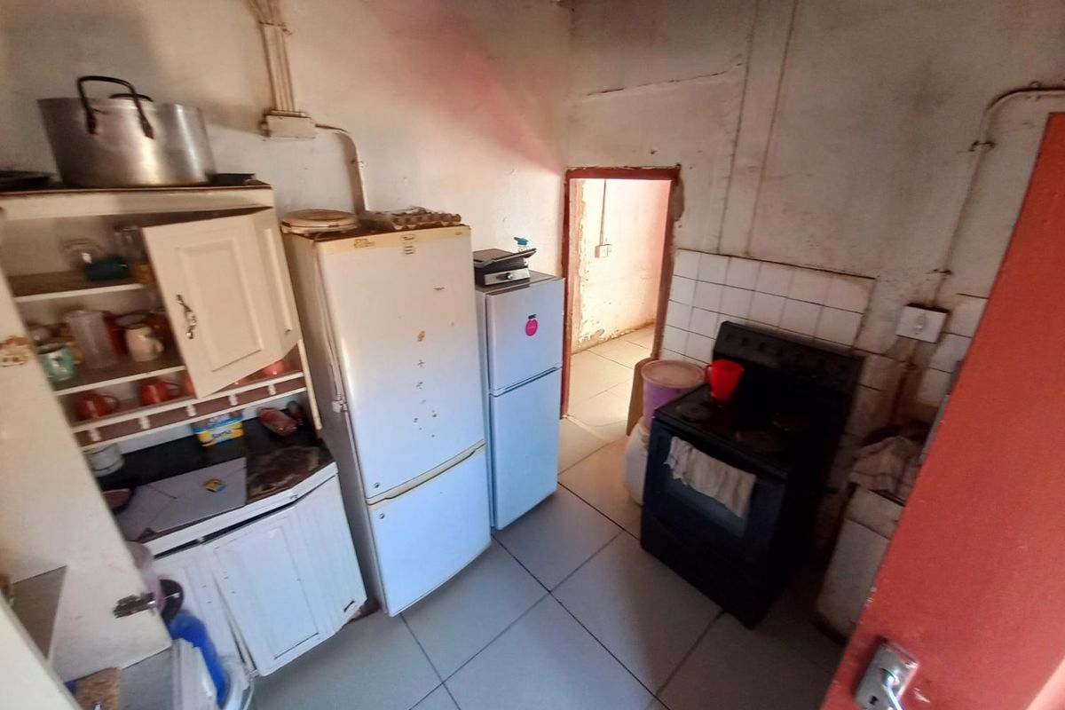 A compact, dated kitchen area featuring tiled flooring, basic cabinetry, and a freestanding stove, requiring significant renovation and cosmetic updates.