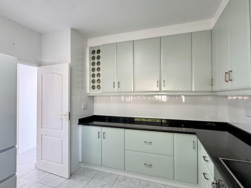A clean, functional kitchen featuring light-colored cabinetry, black granite countertops, tiled backsplash, and integrated storage solutions.