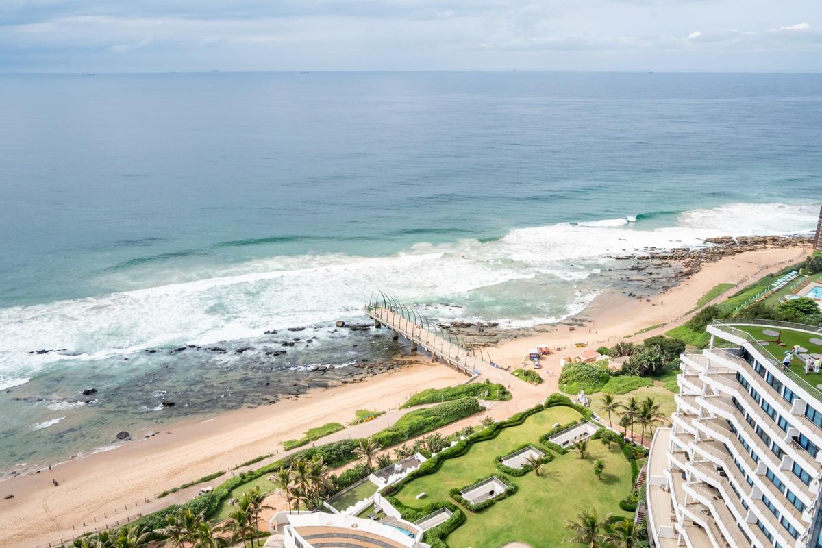An elevated aerial view showcasing the coastal landscape, beach, pier, and surrounding apartment complex infrastructure.