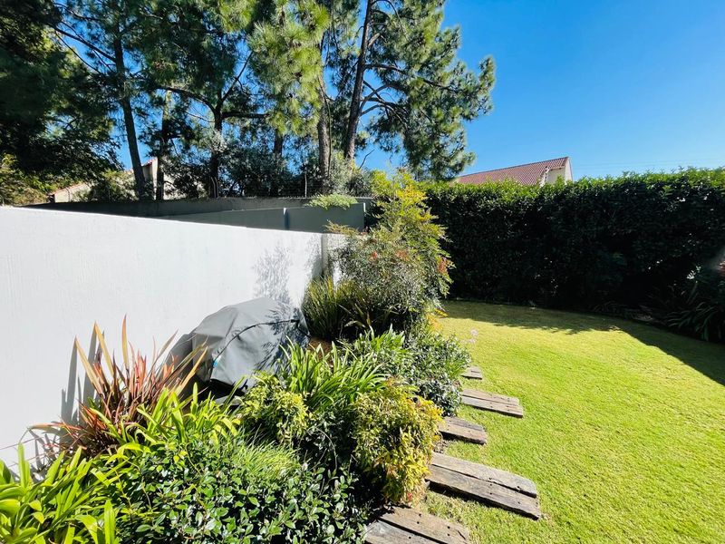 A well-maintained private garden featuring a lush lawn, established perimeter hedging, boundary walls, and a rustic timber sleeper pathway.