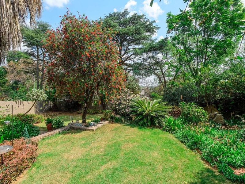 A lush, well-established garden featuring a manicured lawn, mature trees, and stone retaining walls, providing a private and serene outdoor space.