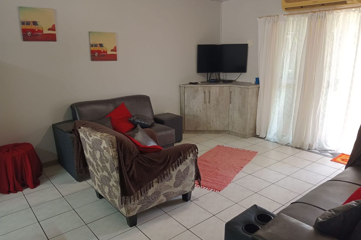 A living room featuring tiled flooring, a wall-mounted air conditioning unit, and a sliding glass door providing access to the exterior.