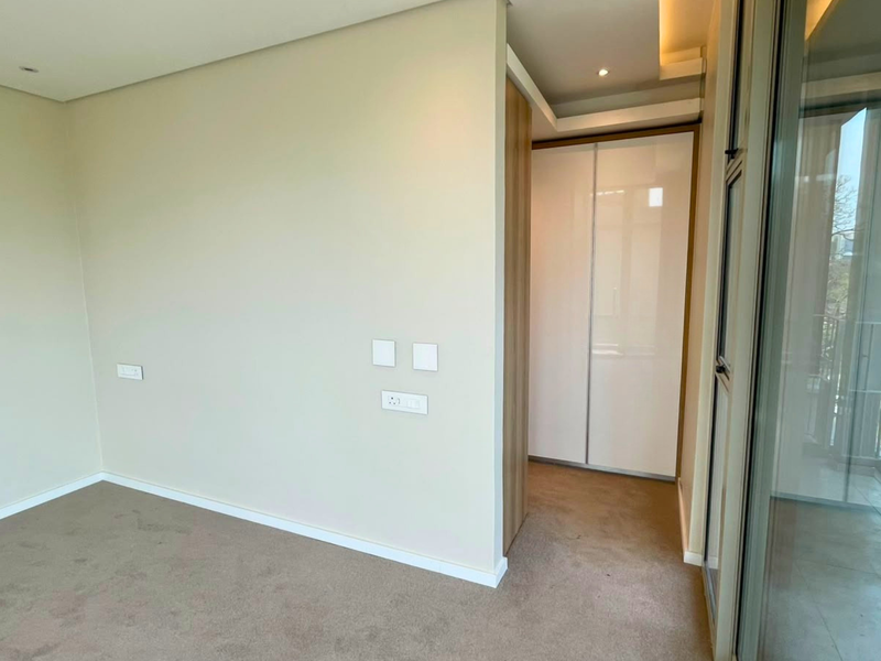 A bright, modern bedroom featuring neutral walls, plush carpeting, built-in wardrobe storage, and a large sliding glass door leading to an outdoor balcony.