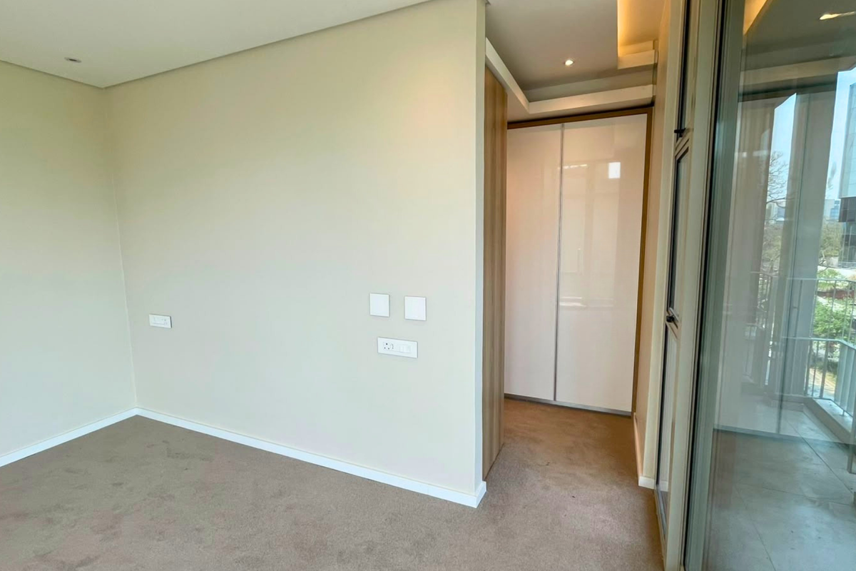 A bright, modern bedroom featuring neutral walls, plush carpeting, built-in wardrobe storage, and a large sliding glass door leading to an outdoor balcony.