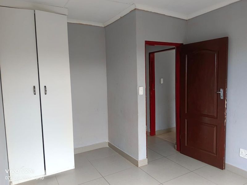 An empty bedroom featuring tiled flooring and a built-in wardrobe, requiring minor cosmetic updates to the door frames and wall finishes.