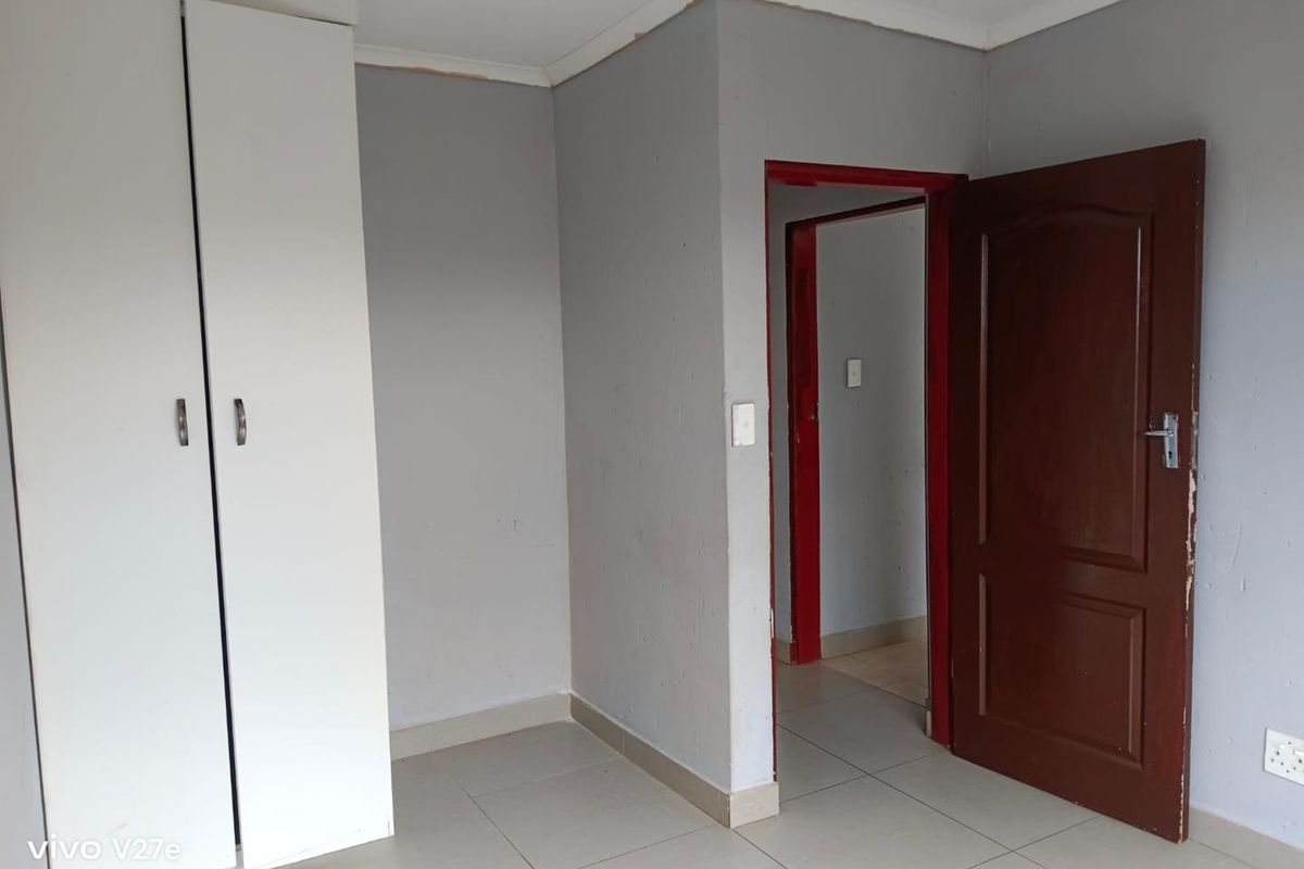 An empty bedroom featuring tiled flooring and a built-in wardrobe, requiring minor cosmetic updates to the door frames and wall finishes.