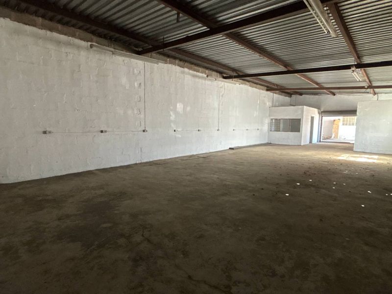 Spacious industrial utility area featuring exposed steel roof trusses, concrete flooring, and painted masonry walls with surface-mounted electrical conduits.
