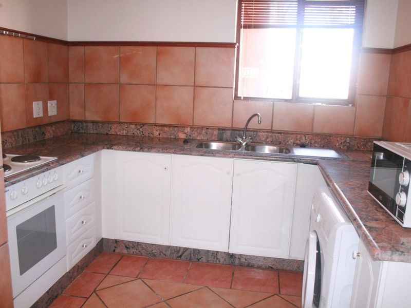 A functional kitchen featuring granite countertops, built-in oven and hob, double sink, and tiled finishes throughout.