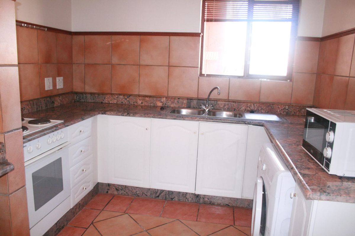 A functional kitchen featuring granite countertops, built-in oven and hob, double sink, and tiled finishes throughout.