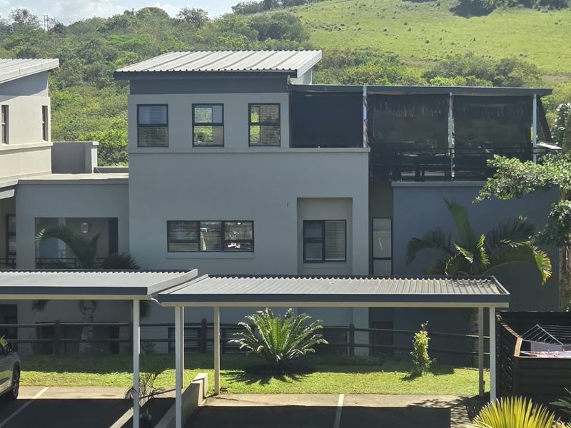 Exterior view of a modern apartment complex featuring covered carports, metal roofing, and balcony access set against a scenic green landscape.