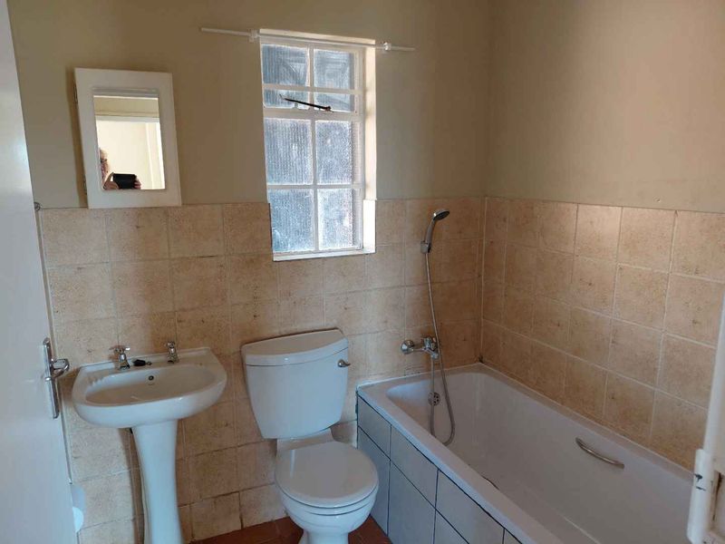 A functional bathroom featuring a pedestal basin, toilet, and bathtub with a handheld shower mixer, finished with tiled wall splashbacks.