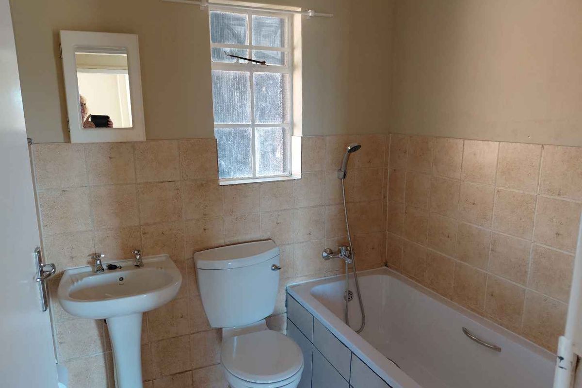A functional bathroom featuring a pedestal basin, toilet, and bathtub with a handheld shower mixer, finished with tiled wall splashbacks.