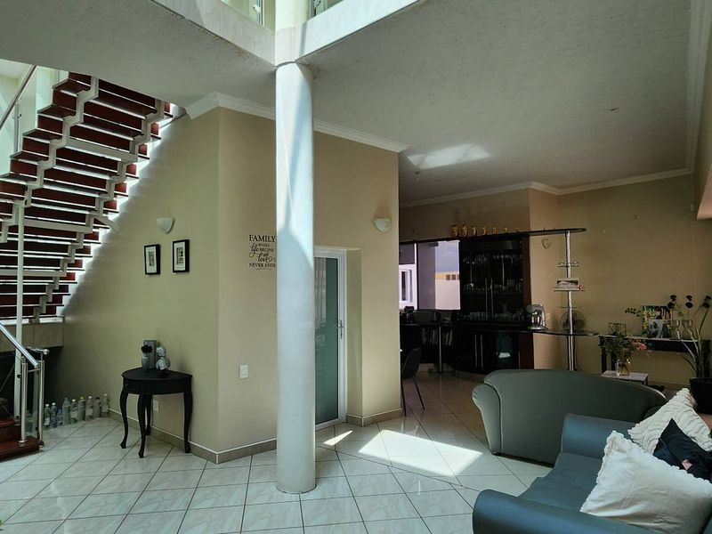 Spacious open-plan living area featuring a prominent staircase with stainless steel balustrades, tiled flooring, and double-volume ceilings with abundant natural light.
