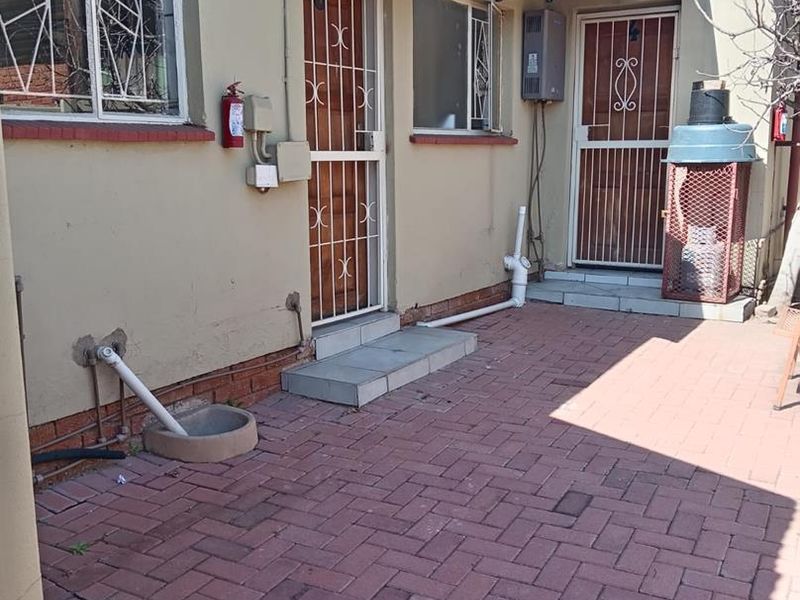 Rear exterior area featuring brick paving, security gates on doors, window security bars, and an installed gas geyser unit.