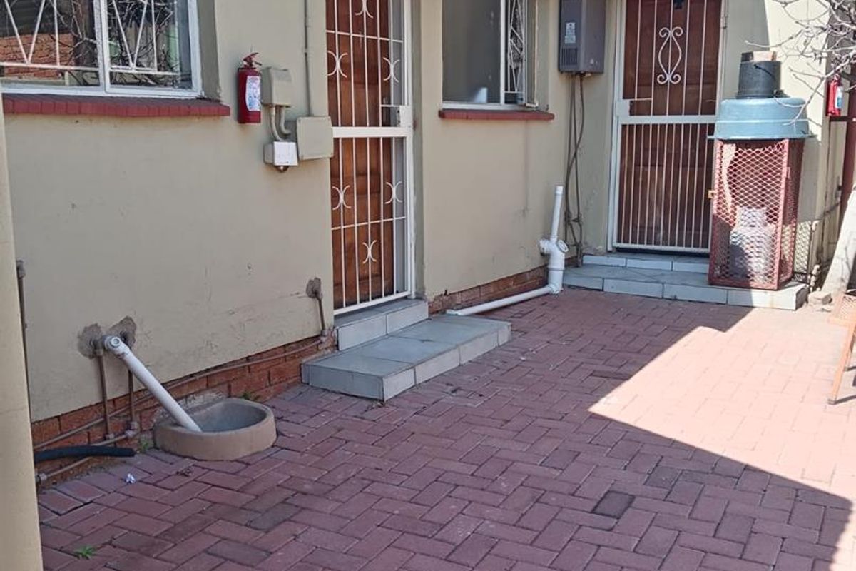 Rear exterior area featuring brick paving, security gates on doors, window security bars, and an installed gas geyser unit.