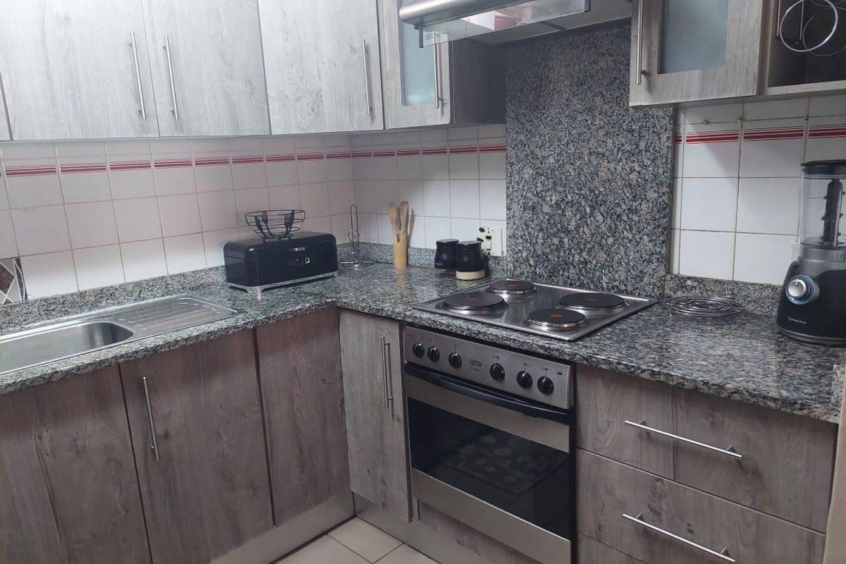 A functional kitchen featuring granite countertops, built-in oven, electric hob, extractor fan, and modern wood-look cabinetry with a tiled backsplash.