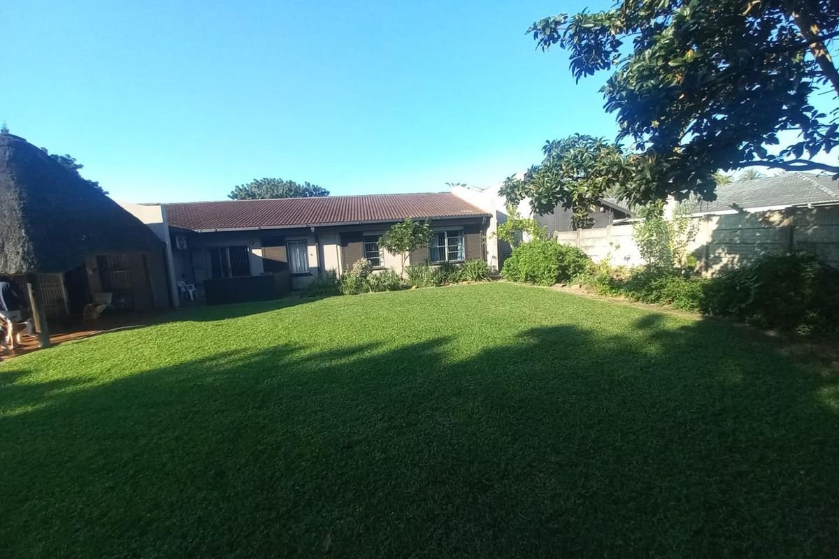 A spacious rear garden featuring a well-maintained lawn, a thatched lapa area, and secure boundary walling.