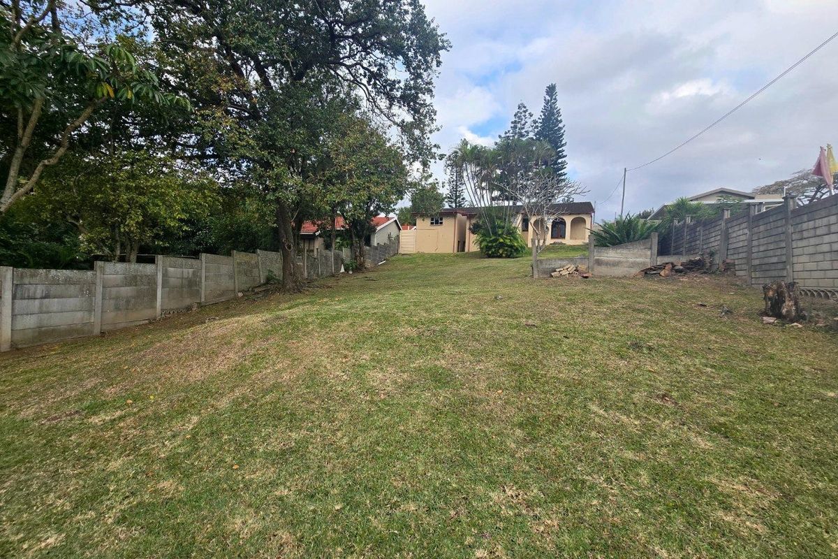 A spacious, sloped rear garden featuring mature trees and concrete boundary walls, providing a private outdoor area behind the main residence.