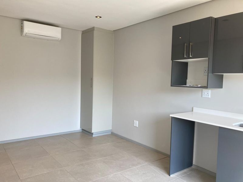 A modern, empty open-plan living and kitchen area featuring neutral tiled floors, built-in cabinetry, and a wall-mounted air conditioning unit.