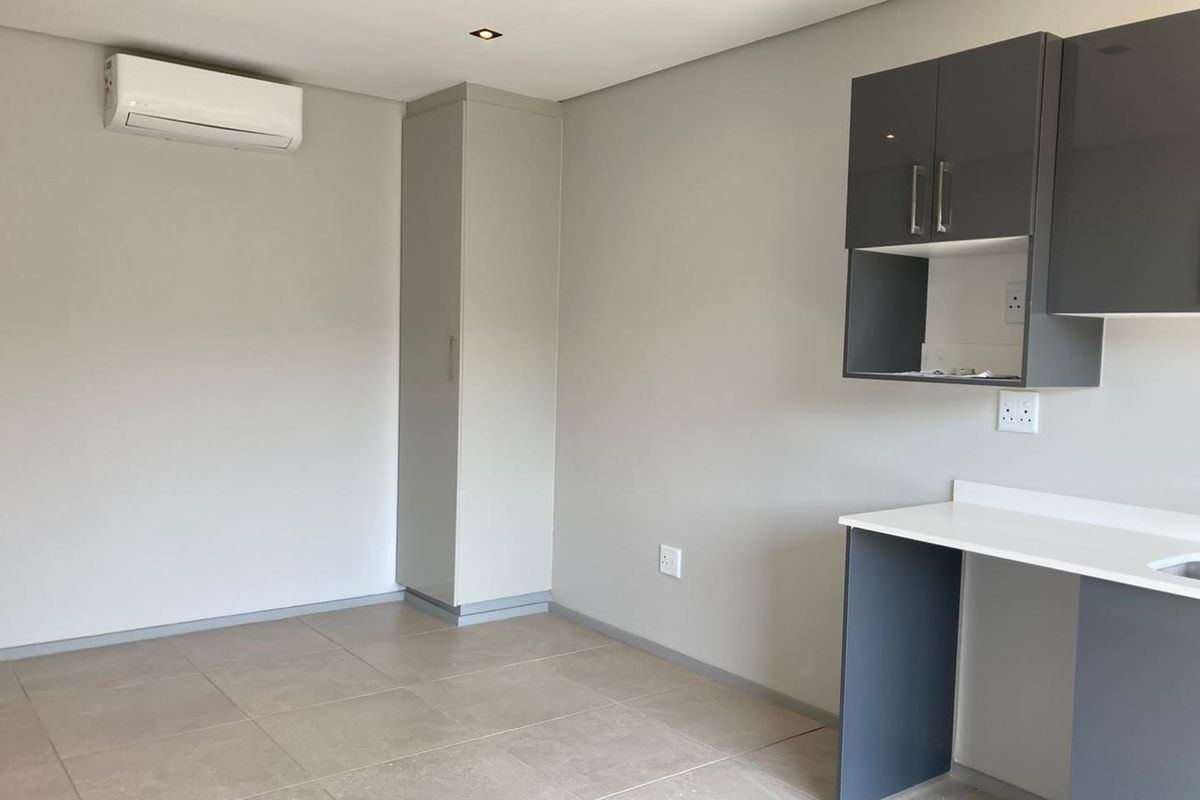 A modern, empty open-plan living and kitchen area featuring neutral tiled floors, built-in cabinetry, and a wall-mounted air conditioning unit.